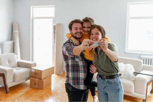 Drei Personen stehen in einem Wohnzimmer mit Umzugskartons und halten einen Schlüssel in den Händen.